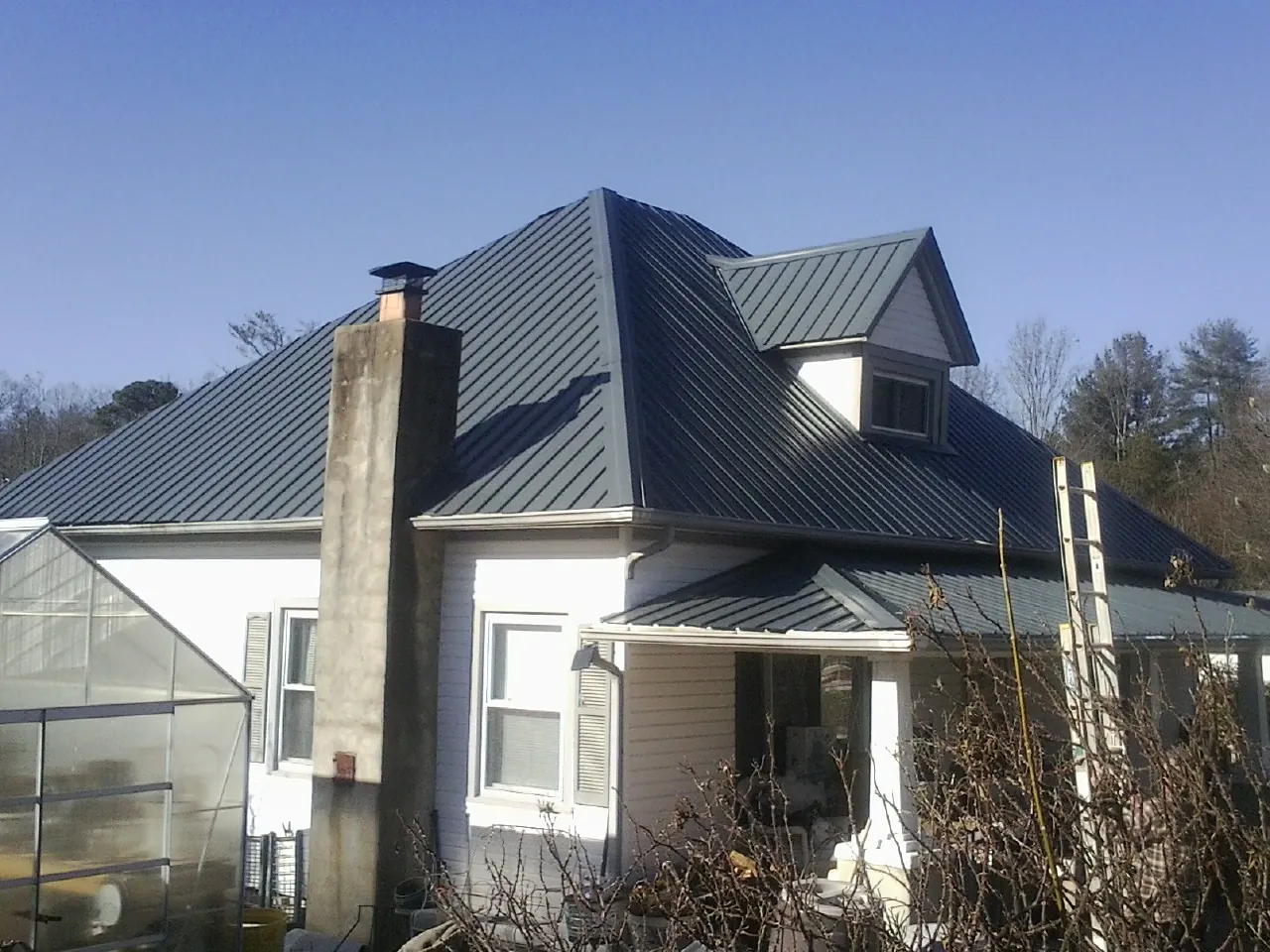 Dark blue standing seam metal roof on a white farmhouse with dormer — Slate & Tile Roof Repair by Roofing Brothers in Douglas