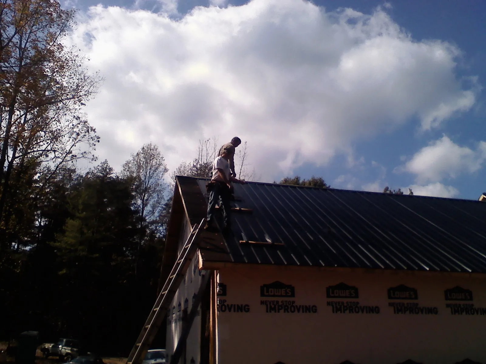 Roofer fastening dark metal panels high against a cloudy sky, from a Roof Inspection job in Douglas
